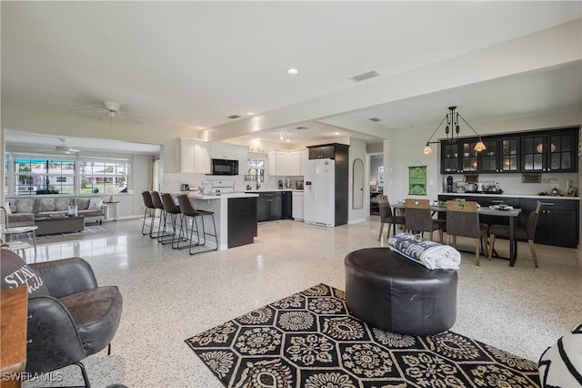 living area featuring baseboards, visible vents, a ceiling fan, light speckled floor, and recessed lighting