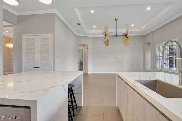 kitchen with light tile patterned flooring, sink, light stone counters, and a tray ceiling