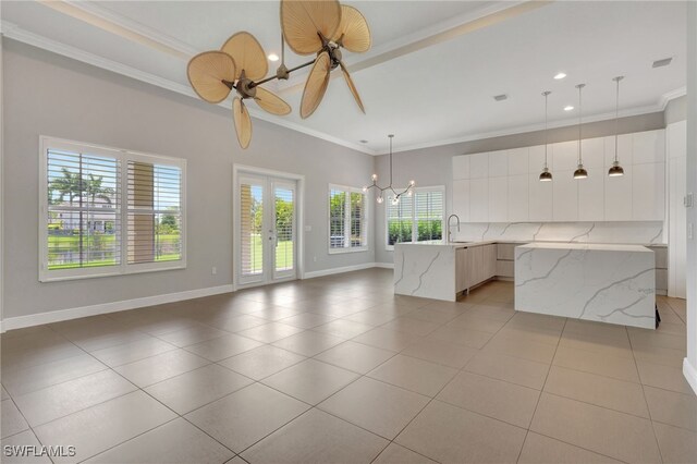 kitchen featuring light tile patterned flooring, light stone counters, an island with sink, white cabinetry, and hanging light fixtures