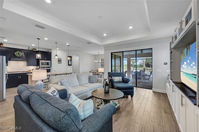 living room with crown molding, a raised ceiling, and an inviting chandelier