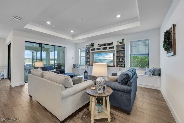 living room featuring a tray ceiling, visible vents, wood finished floors, and ornamental molding