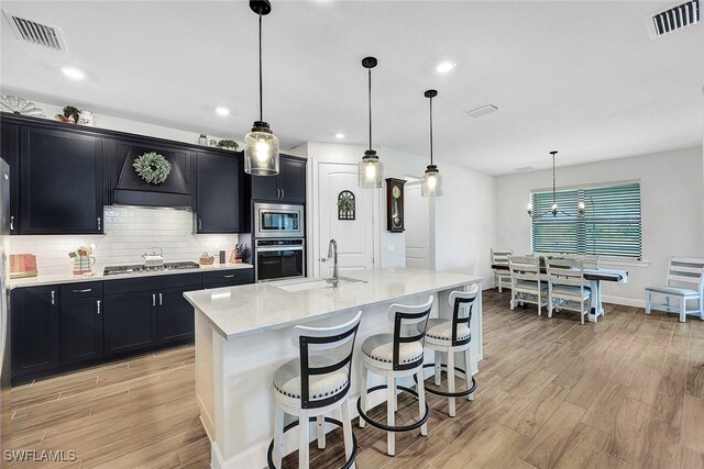 kitchen featuring dark cabinetry, visible vents, a sink, light wood-style floors, and appliances with stainless steel finishes