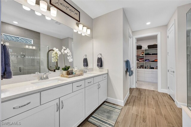 bathroom with a walk in closet, wood finish floors, double vanity, a stall shower, and a sink