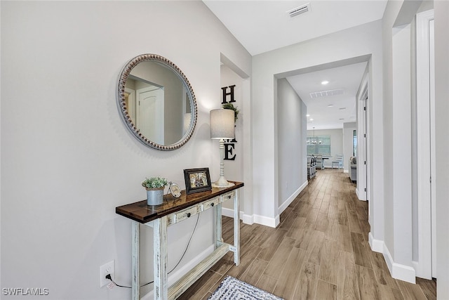 corridor with hardwood / wood-style floors and an inviting chandelier