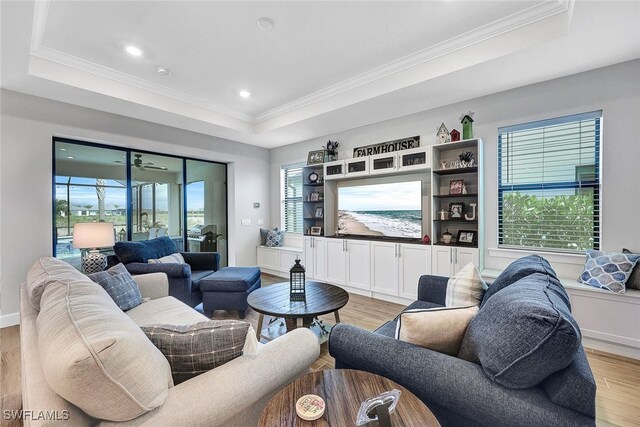 living room featuring a healthy amount of sunlight, light wood-style flooring, a tray ceiling, and ornamental molding