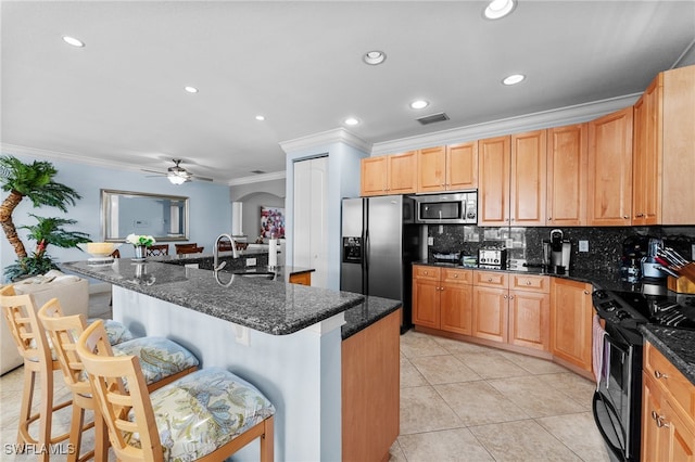 kitchen featuring stainless steel appliances, an island with sink, dark stone counters, a breakfast bar area, and ceiling fan