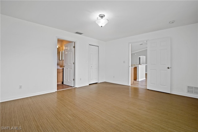 unfurnished bedroom with ensuite bath and wood-type flooring