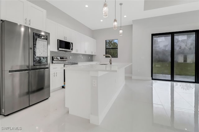 kitchen with appliances with stainless steel finishes, backsplash, an island with sink, pendant lighting, and white cabinets