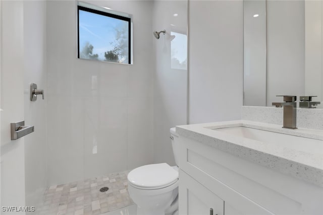 bathroom with toilet, a tile shower, and vanity