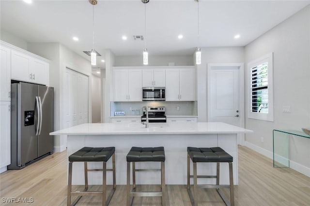 kitchen featuring backsplash, a kitchen bar, light countertops, stainless steel appliances, and white cabinetry