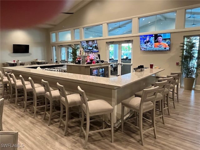 bar with french doors, high vaulted ceiling, and light hardwood / wood-style floors