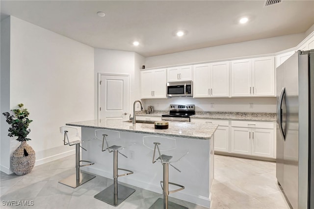 kitchen with white cabinets, light stone counters, appliances with stainless steel finishes, a kitchen breakfast bar, and a sink