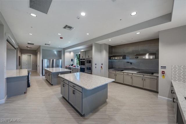 kitchen featuring gray cabinetry, a center island, light stone counters, decorative backsplash, and exhaust hood