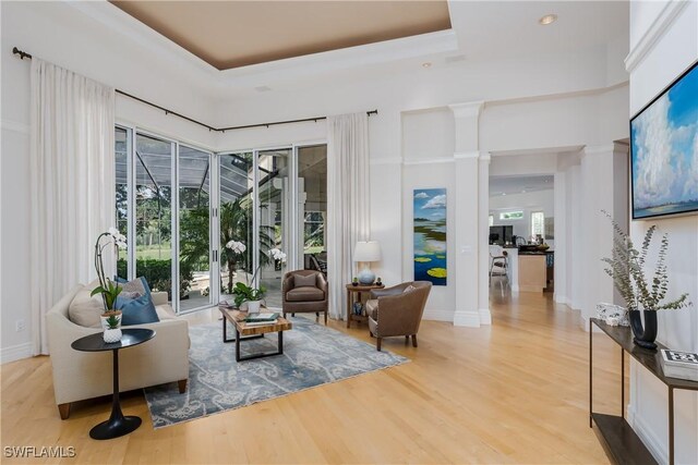 living room featuring decorative columns, light hardwood / wood-style floors, and a raised ceiling