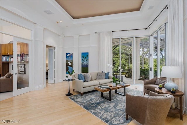 living area with visible vents, a towering ceiling, wood finished floors, a tray ceiling, and french doors