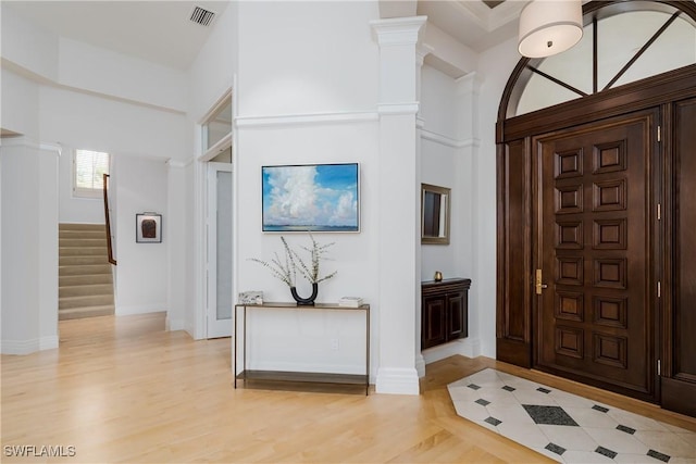 foyer entrance with decorative columns, visible vents, light wood-style flooring, stairway, and baseboards