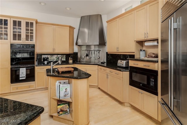 kitchen featuring dark stone counters, glass insert cabinets, wall chimney range hood, a center island, and black appliances