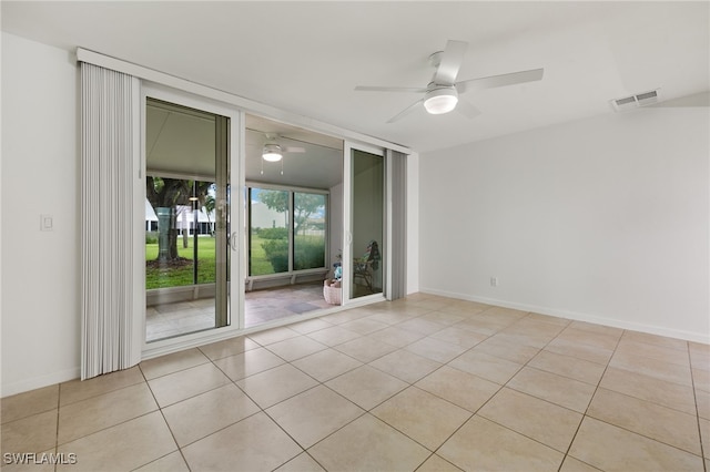 tiled spare room featuring ceiling fan, visible vents, baseboards, and expansive windows