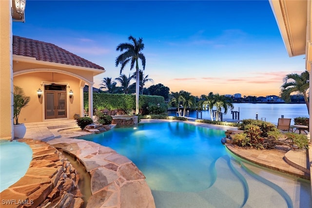 pool at dusk featuring a water view, french doors, a jacuzzi, and a patio area