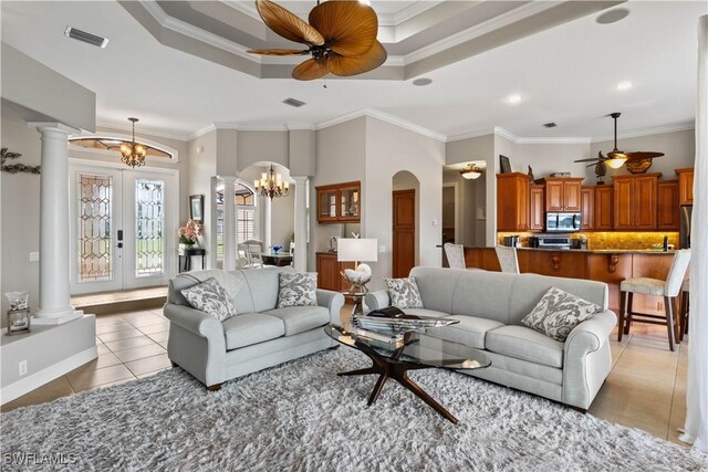 living room with ornate columns, ornamental molding, ceiling fan with notable chandelier, and light tile patterned floors