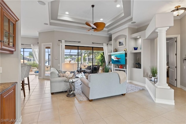 living area featuring built in shelves, a tray ceiling, decorative columns, and a ceiling fan