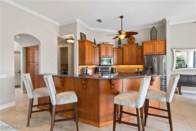 kitchen featuring ceiling fan, decorative backsplash, a breakfast bar, appliances with stainless steel finishes, and light tile patterned floors