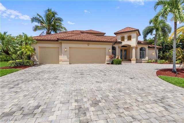 mediterranean / spanish-style house with decorative driveway, a tile roof, an attached garage, and stucco siding