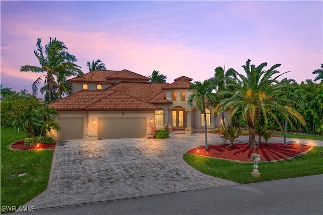 mediterranean / spanish-style home with a front lawn, decorative driveway, an attached garage, and stucco siding