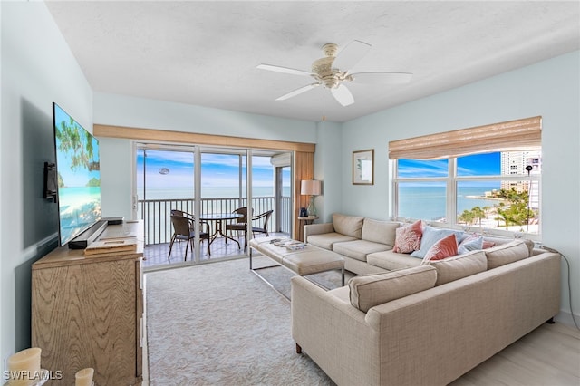 carpeted living room with ceiling fan, a healthy amount of sunlight, and a water view