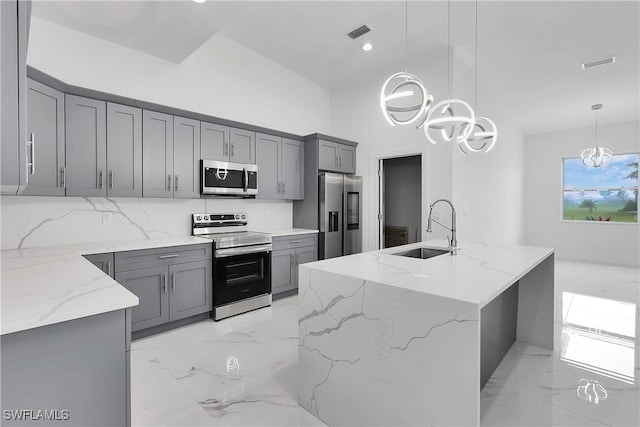 kitchen with light stone countertops, stainless steel appliances, hanging light fixtures, and sink