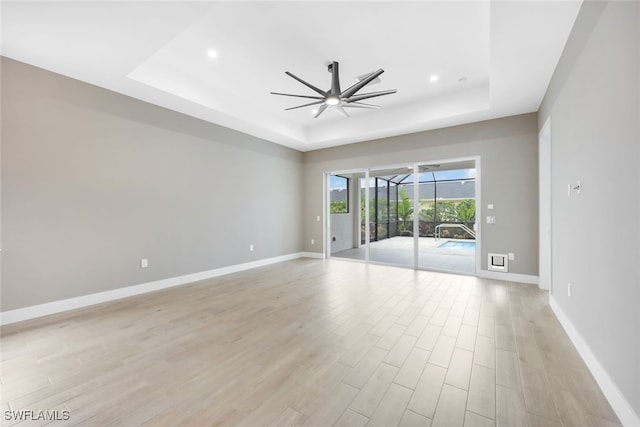 empty room with light wood-type flooring, a raised ceiling, and ceiling fan