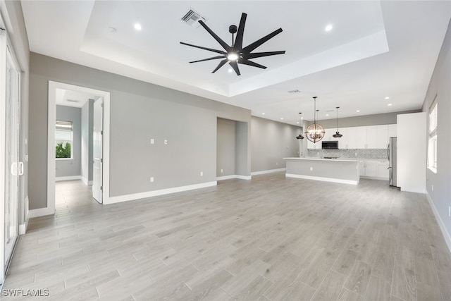 unfurnished living room with ceiling fan with notable chandelier, light hardwood / wood-style floors, and a raised ceiling