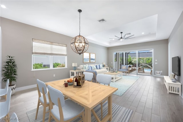 dining room featuring wood-type flooring, ceiling fan with notable chandelier, and a tray ceiling