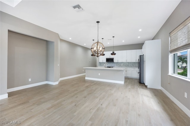 kitchen with light wood-type flooring, stainless steel appliances, a kitchen island with sink, decorative light fixtures, and white cabinetry