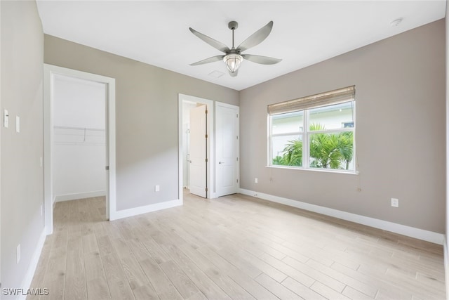 unfurnished bedroom featuring a closet, light hardwood / wood-style floors, a spacious closet, and ceiling fan