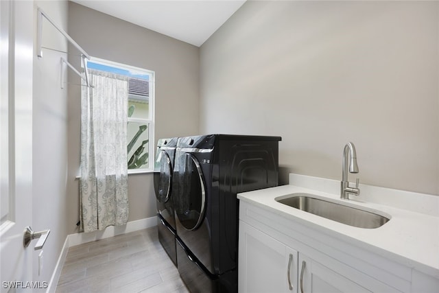 clothes washing area with separate washer and dryer, sink, cabinets, and light wood-type flooring