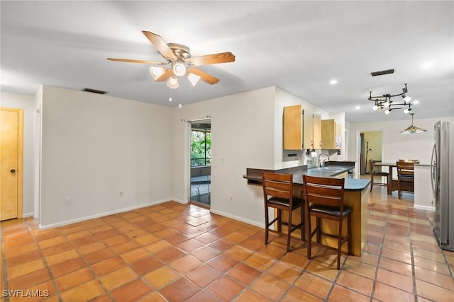 kitchen with light tile patterned floors, visible vents, dark countertops, freestanding refrigerator, and a sink