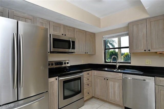 kitchen with stainless steel appliances, a tray ceiling, sink, and light brown cabinets