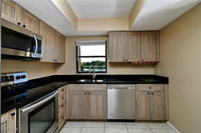 kitchen with sink, a raised ceiling, appliances with stainless steel finishes, and light tile patterned flooring