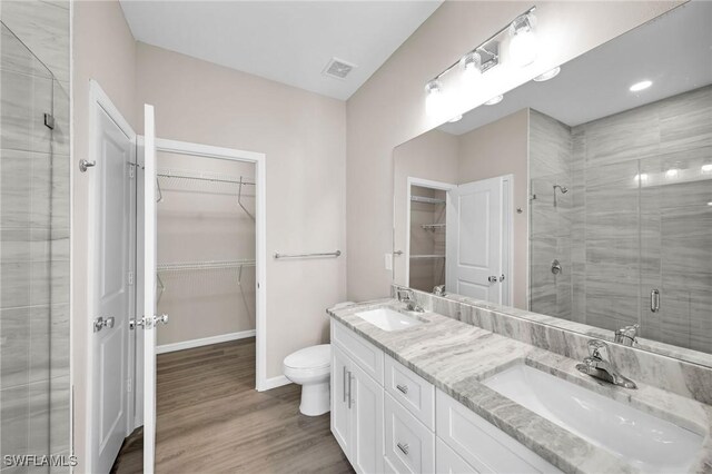 bathroom with hardwood / wood-style floors, a shower with door, double sink vanity, and toilet