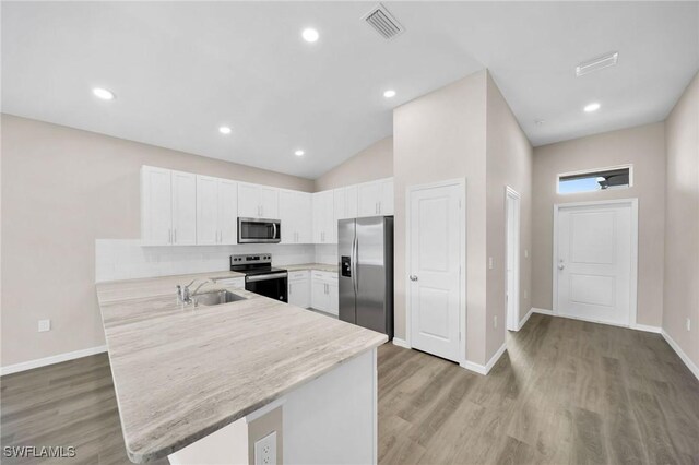 kitchen featuring appliances with stainless steel finishes, white cabinets, tasteful backsplash, light hardwood / wood-style floors, and kitchen peninsula