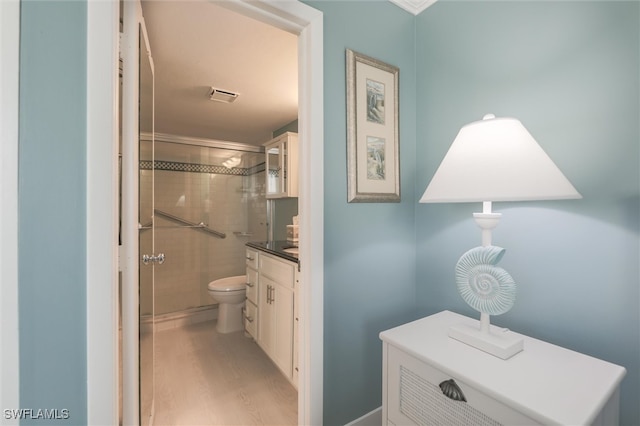 bathroom with toilet, crown molding, vanity, tiled shower, and hardwood / wood-style flooring