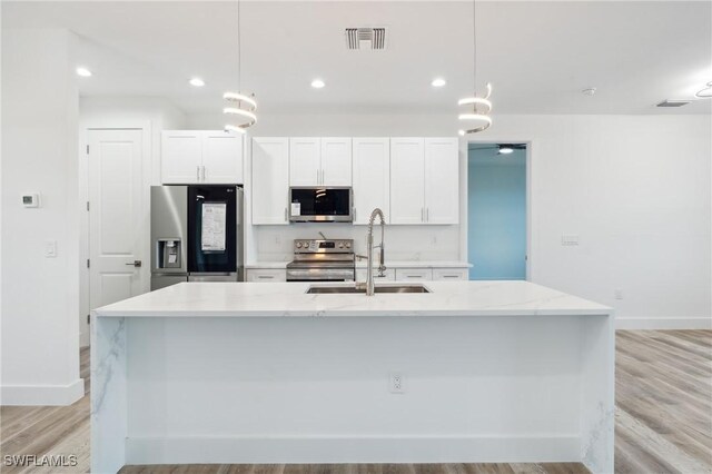 kitchen featuring appliances with stainless steel finishes, light hardwood / wood-style flooring, a center island with sink, and decorative light fixtures