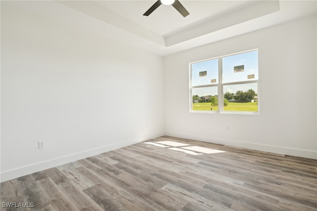 empty room featuring ceiling fan, wood-type flooring, and a tray ceiling