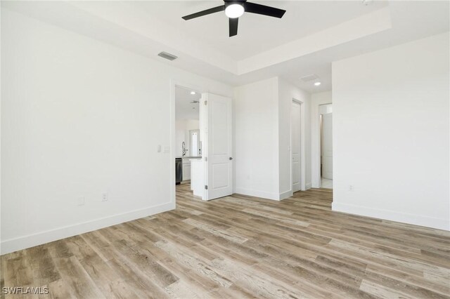 interior space featuring ceiling fan, a raised ceiling, and light hardwood / wood-style flooring