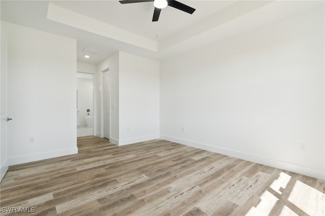 empty room with light hardwood / wood-style floors, a raised ceiling, and ceiling fan