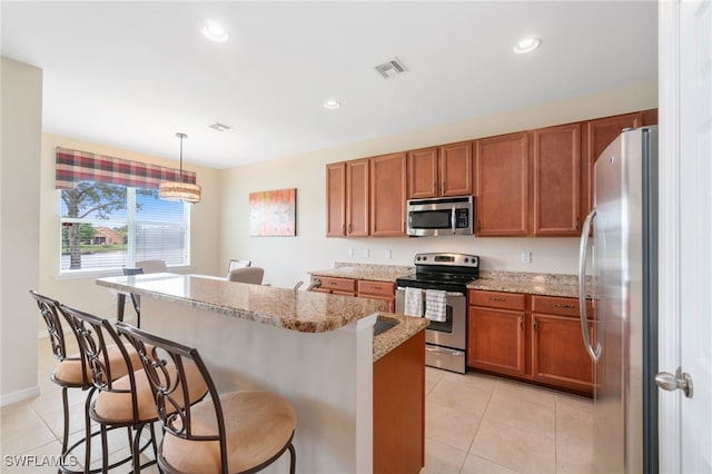 kitchen with light tile patterned flooring, appliances with stainless steel finishes, a kitchen island, and decorative light fixtures