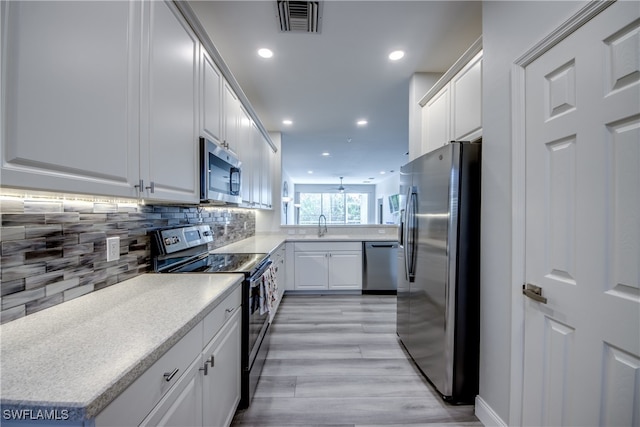 kitchen featuring light wood-type flooring, white cabinetry, appliances with stainless steel finishes, and backsplash