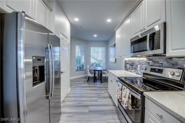 kitchen with white cabinetry, stainless steel appliances, light wood-type flooring, and backsplash