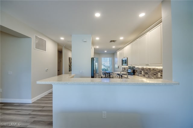 kitchen featuring light wood-type flooring, tasteful backsplash, white cabinets, kitchen peninsula, and stainless steel appliances